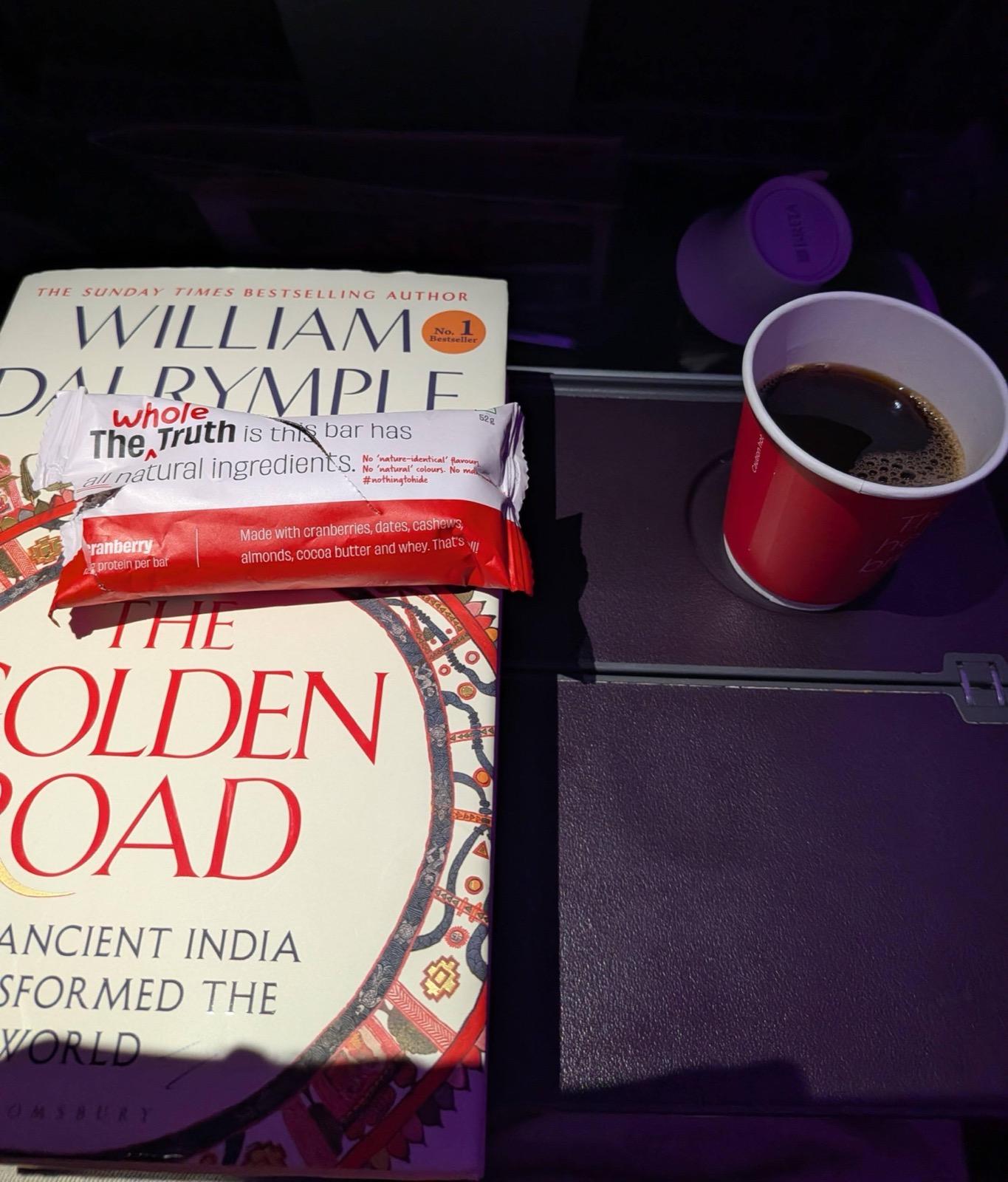 Protein bar, coffee, and a book on a tray table during a flight